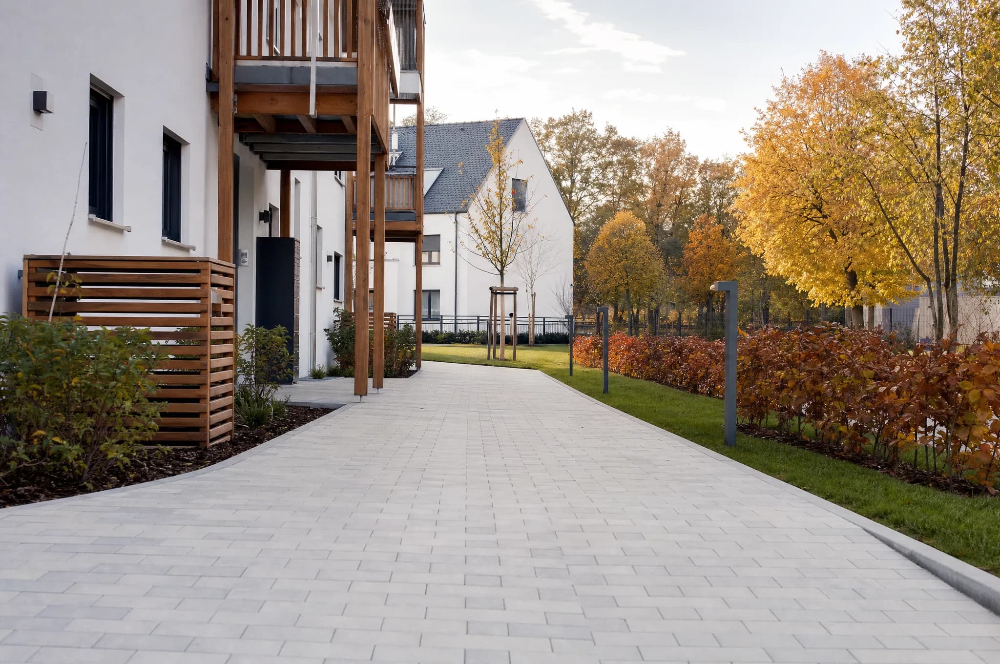 Vom Laub befreiter Gehweg vor einer Wohnanlage im Herbst